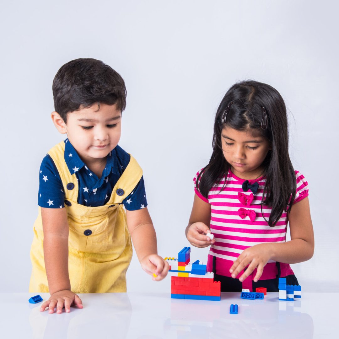 Cute little Indian or asian kids playing with toys or blocks and having fun while sitting at table or isolated over white background Cute little Indian or asian kids playing with toys or blocks and having fun while sitting at table or isolated over white background